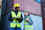 Man and woman, wearing high visibility jackets and hard hats, laughing in front of stacked shipping containers.