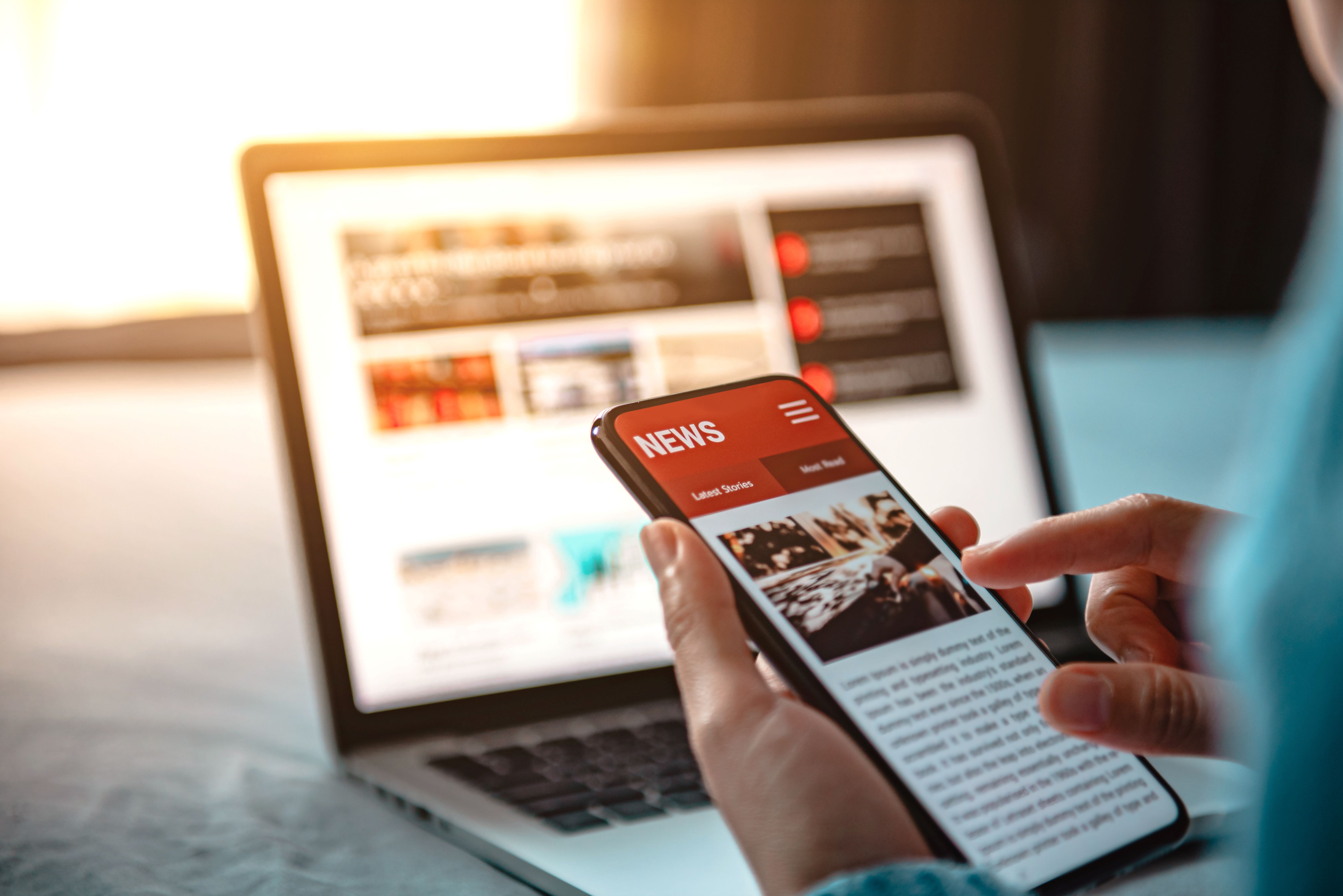 Person reading news on phone and laptop