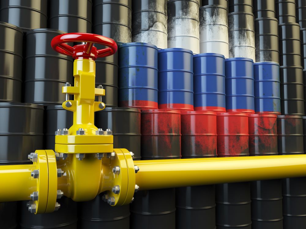 Barrels of oil with Russian flag sprayed on, in front of oil pipeline