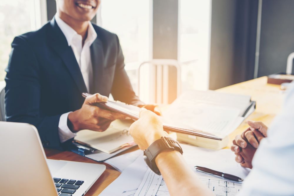 Insurance broker sat at table, handing over papers to client