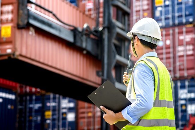 Worker in hard hat and high-visibility vest inspecting shipping container