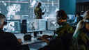 Military figures in a command centre working on a laptop