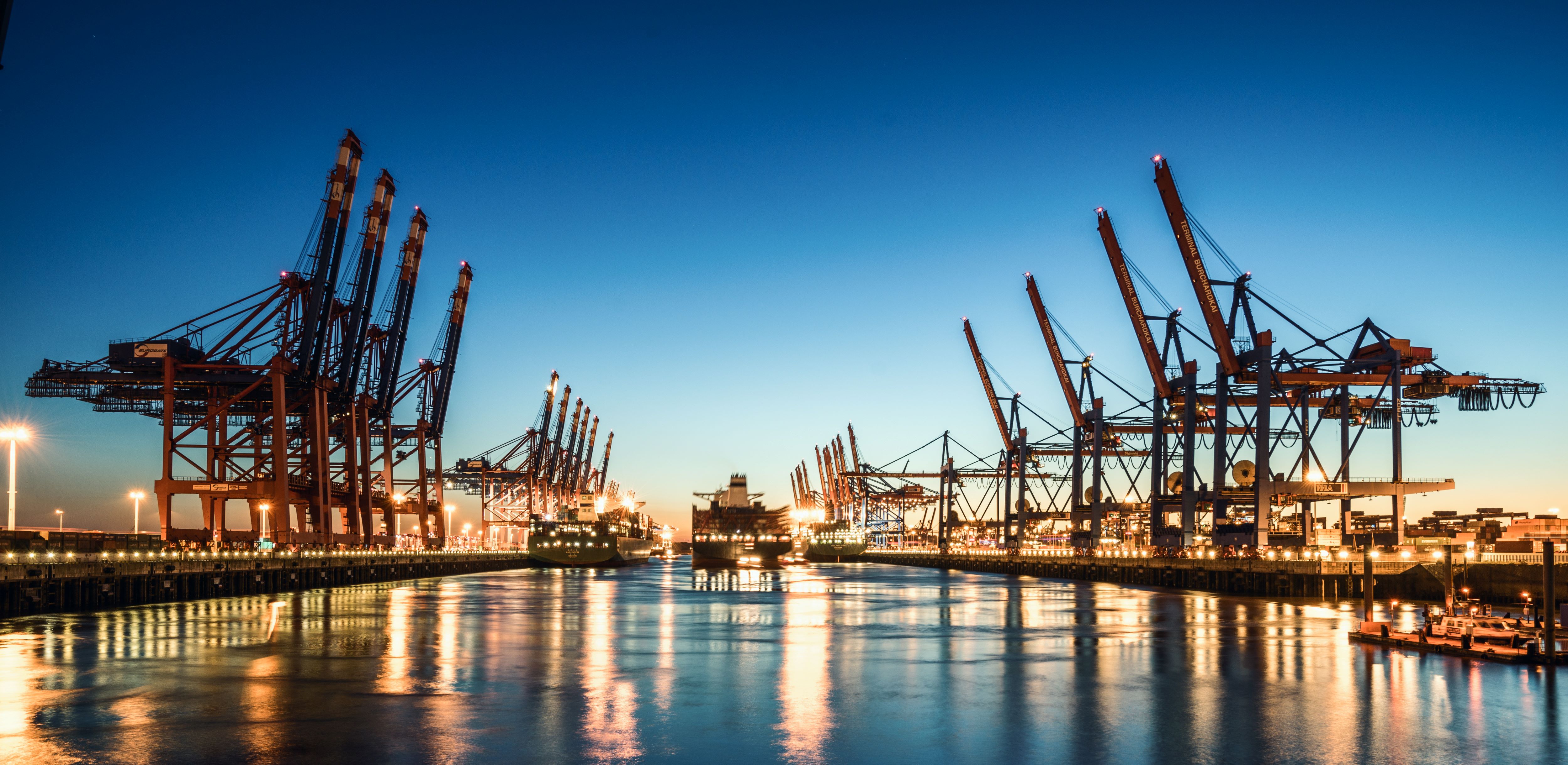 Port of Hamburg at night with ship passing alongside raised cranes